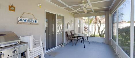 A covered patio with a grill, chairs, and a table.