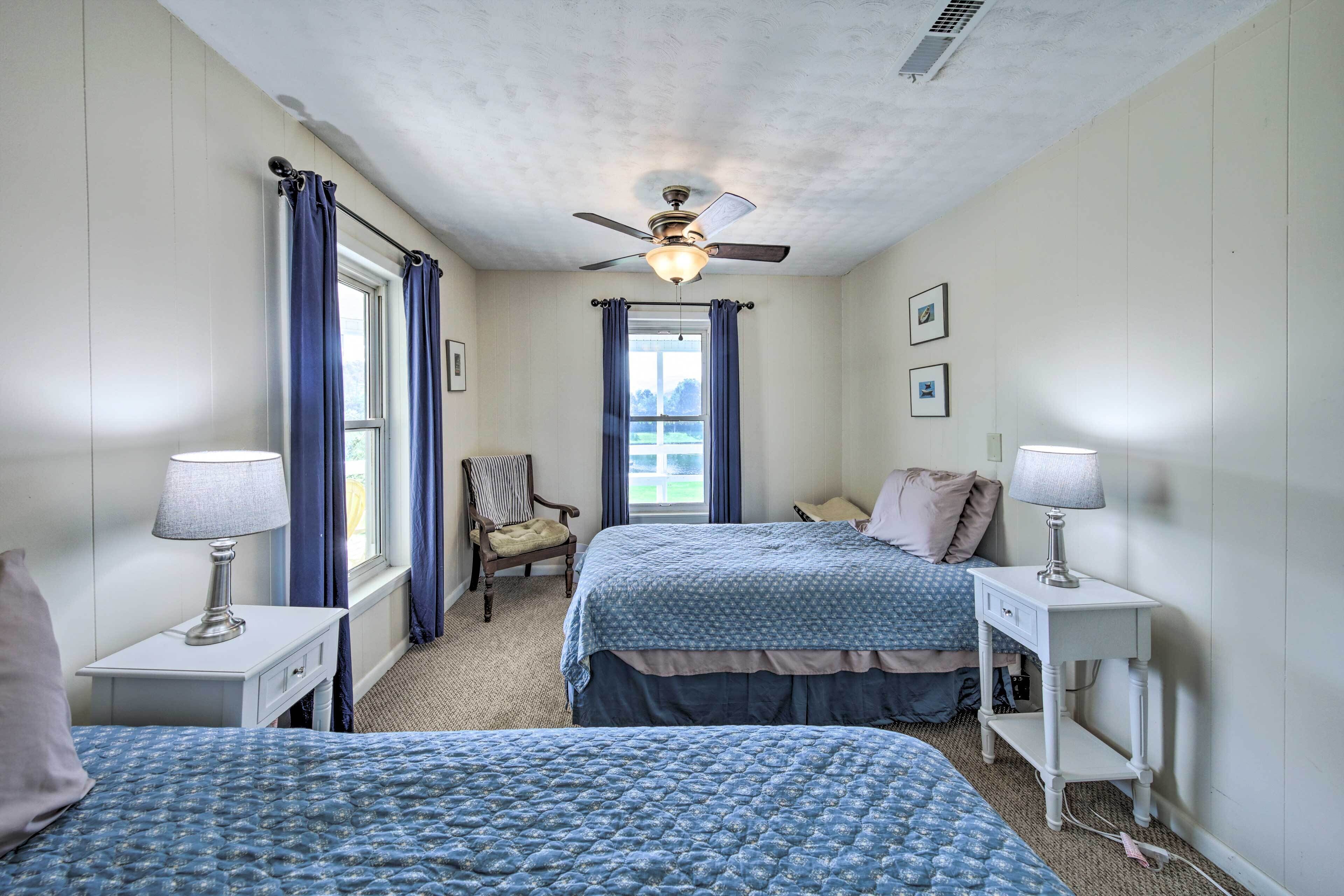 A bedroom with two beds, a ceiling fan, a window with curtains, and a chair.