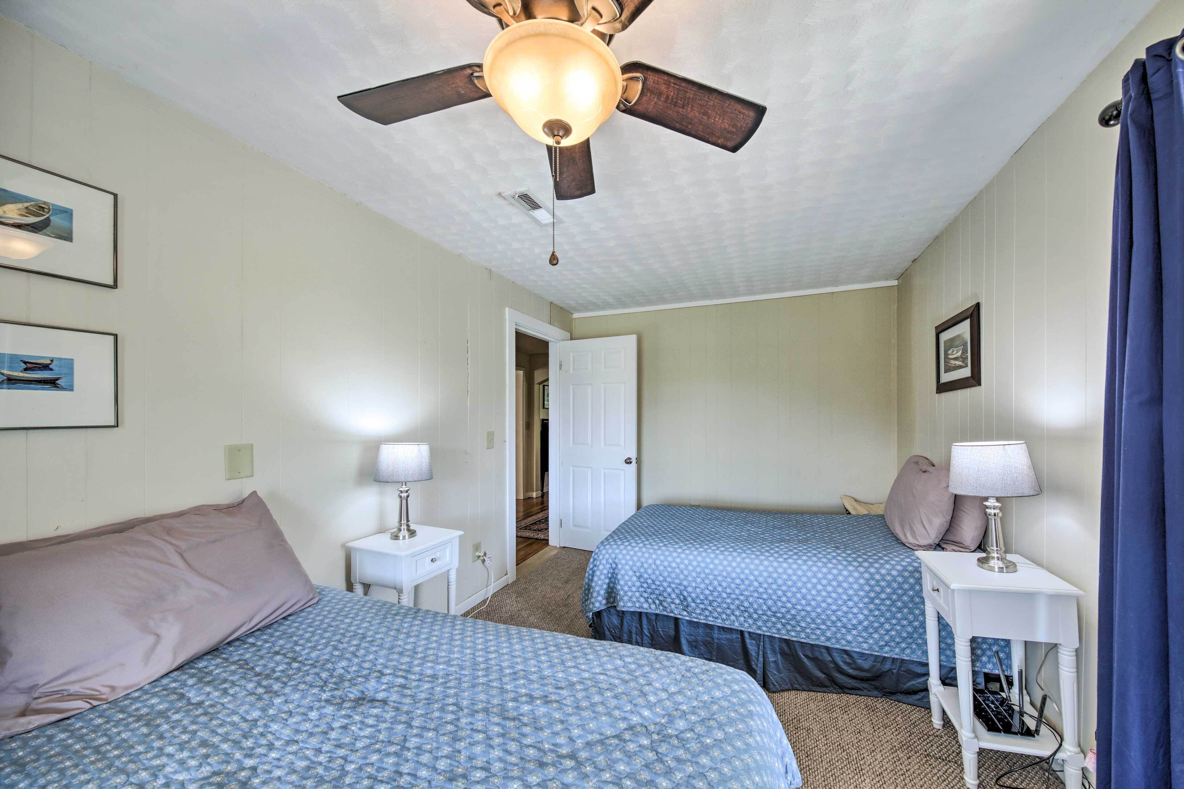 A bedroom with two beds, a ceiling fan, and a door leading to another room.