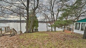 A lakeside property with a wooden deck, a small shed, and a cabin with large windows overlooking the water. - Fire Pit & Grill: Lakeview Mecosta Cottage! (Mecosta)