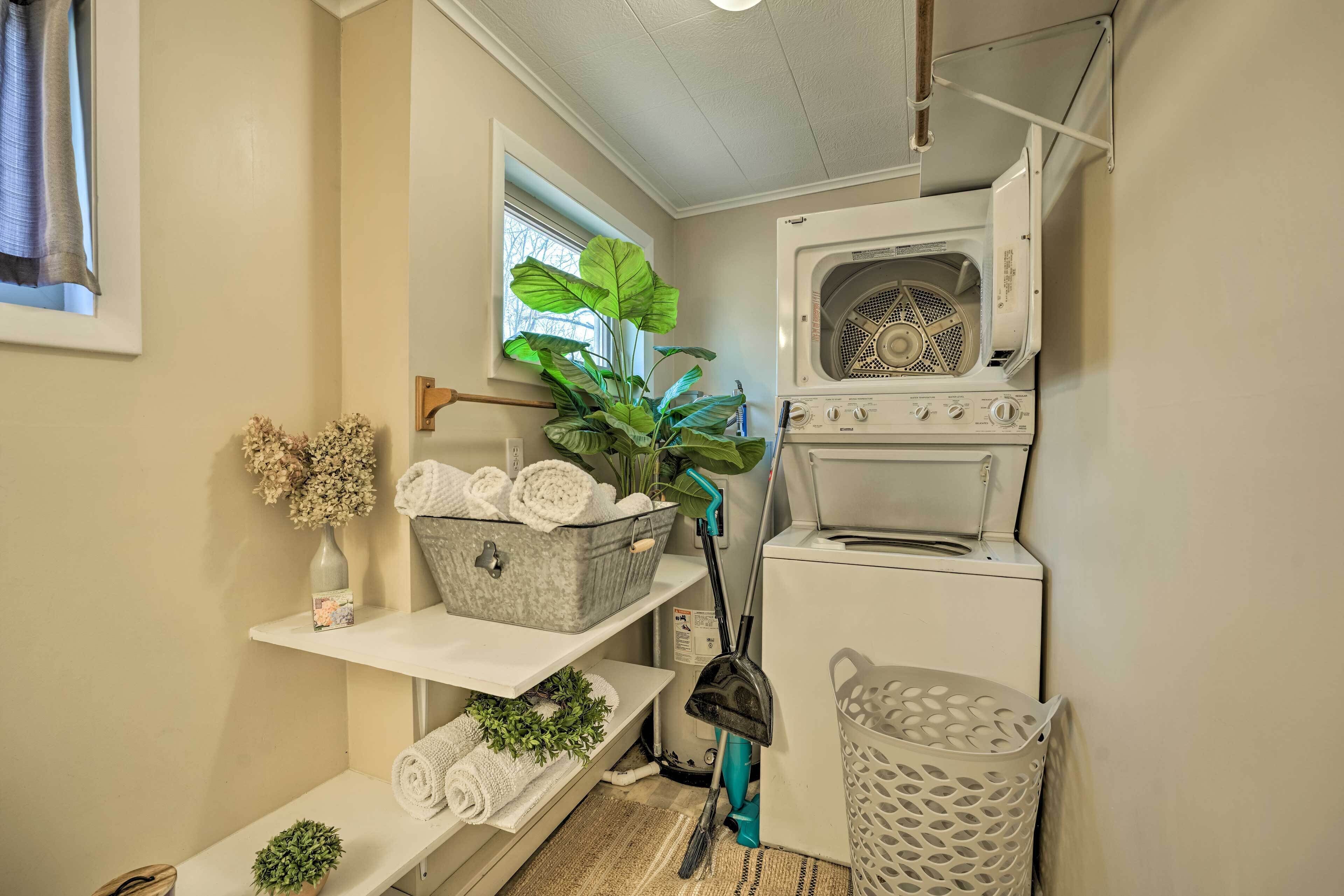 A laundry room with a washing machine, a drying machine, a shelf with folded towels, a potted plant, and a basket.