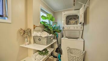 A laundry room with a washing machine, a drying machine, a shelf with folded towels, a potted plant, and a basket.