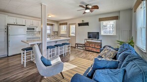 A modern kitchen with white cabinets, a central island with bar stools, a dining table, and a ceiling fan. - Fire Pit & Grill: Lakeview Mecosta Cottage! (Mecosta)