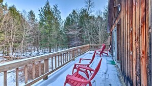 Eine Holzterrasse mit roten Stühlen und einem Holzgeländer, mit Blick auf einen verschneiten Wald.