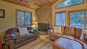 Ein gemütliches Wohnzimmer mit Kamin aus Stein, Ledersofas und großen Fenstern mit Blick auf den Wald.