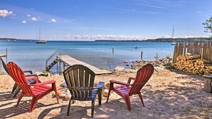 A beach with three Adirondack chairs, a wooden dock, and a view of the sea with boats. - Quaint Studio w/ Shared Beach: Walk to Suttons Bay (Suttons Bay)