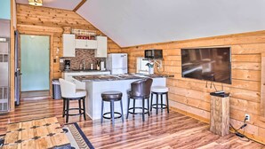 A kitchen with wooden walls, a large island with stools, a TV, and a refrigerator. - Quaint Studio w/ Shared Beach: Walk to Suttons Bay (Suttons Bay)