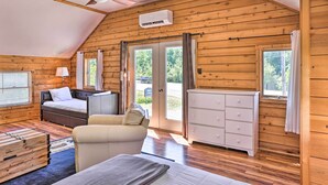 A cozy log cabin bedroom with a bed, a sofa, a dresser, and a ceiling fan. - Quaint Studio w/ Shared Beach: Walk to Suttons Bay (Suttons Bay)