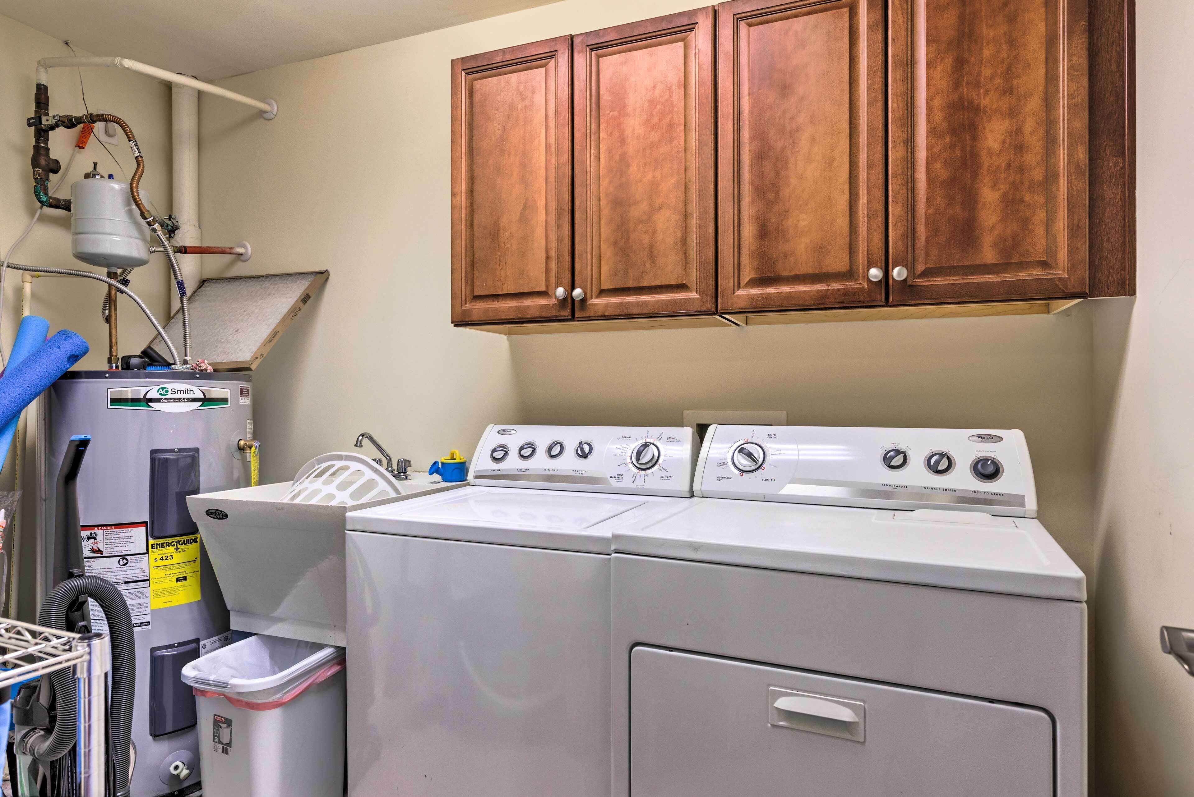 A laundry area with a front-loading washer and dryer, a water heater, and wooden cabinets above.