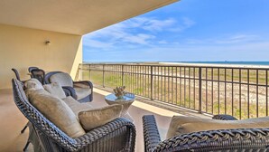 A balcony with wicker furniture, a small table, and a view of the beach. - Family Condo: Resort Pool Access & Ocean View (Dauphin Island)