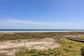 A coastal landscape with a sandy beach, a wooden boardwalk, and a clear blue sky.