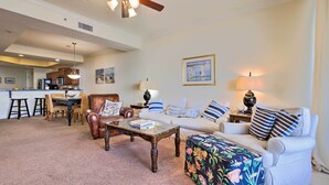 A spacious living room with a dining area, a ceiling fan, and a kitchen in the background. - Family Condo: Resort Pool Access & Ocean View (Dauphin Island)
