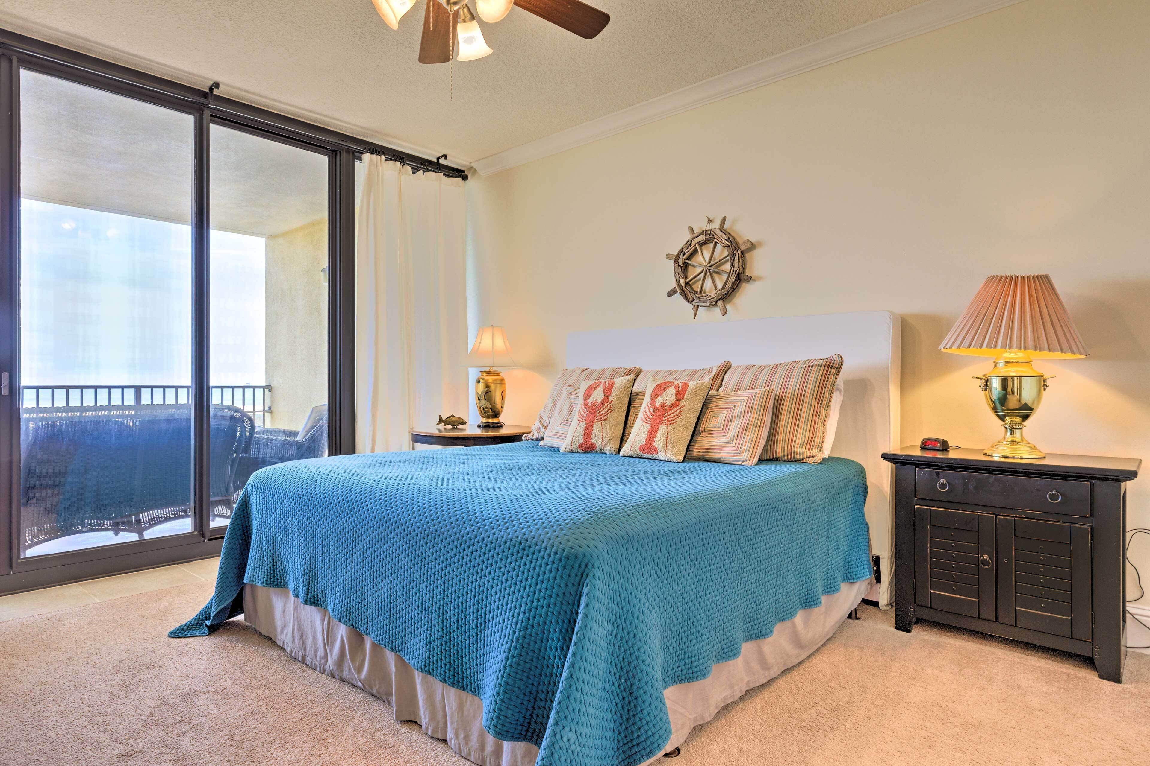 A bedroom with a large bed, a nightstand, a lamp, a wall clock, and a view through a sliding door.