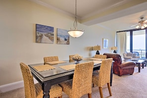 A dining area with a dark wooden table, woven chairs, and a hanging light fixture. - Family Condo: Resort Pool Access & Ocean View (Dauphin Island)
