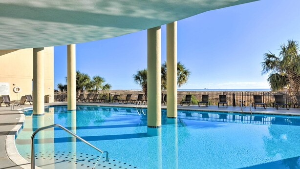 A swimming pool with lounge chairs and palm trees. - Family Condo: Resort Pool Access & Ocean View (Dauphin Island)