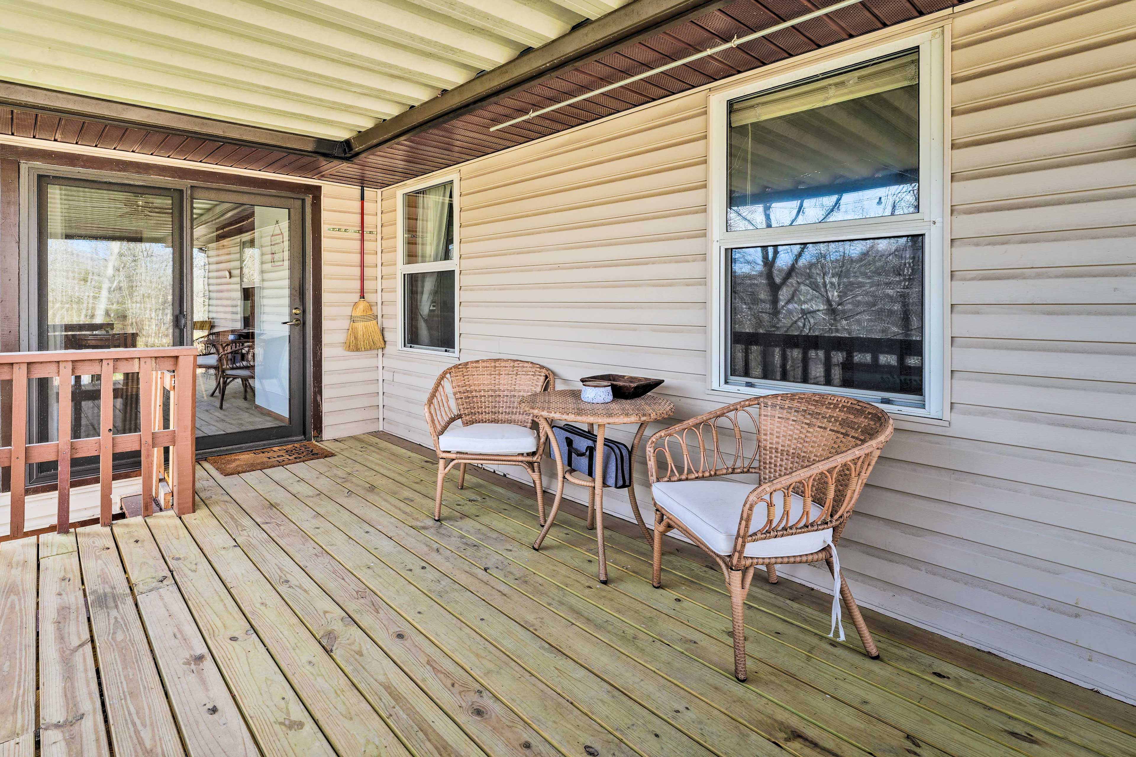 A wooden deck with wicker chairs and a small table, a sliding glass door, and a covered porch area.