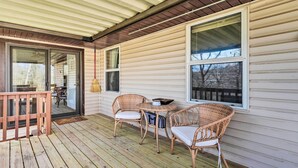 A wooden deck with wicker chairs and a small table, a sliding glass door, and a covered porch area.