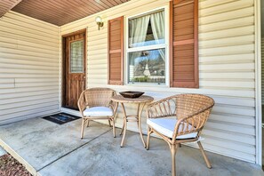 A porch with two wicker chairs and a small table, a wooden door, and a window with curtains. - Missouri Retreat ~ 7 Mi to Silver Dollar City (Branson West)