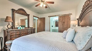 A bedroom with a large bed, a wooden dresser, a mirror, and a ceiling fan.