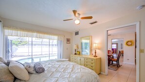 Quarto com uma cama grande, um ventilador de teto, cômoda e janela com cortinas.