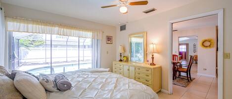 A bedroom with a large bed, a ceiling fan, a dresser, and a window with curtains.