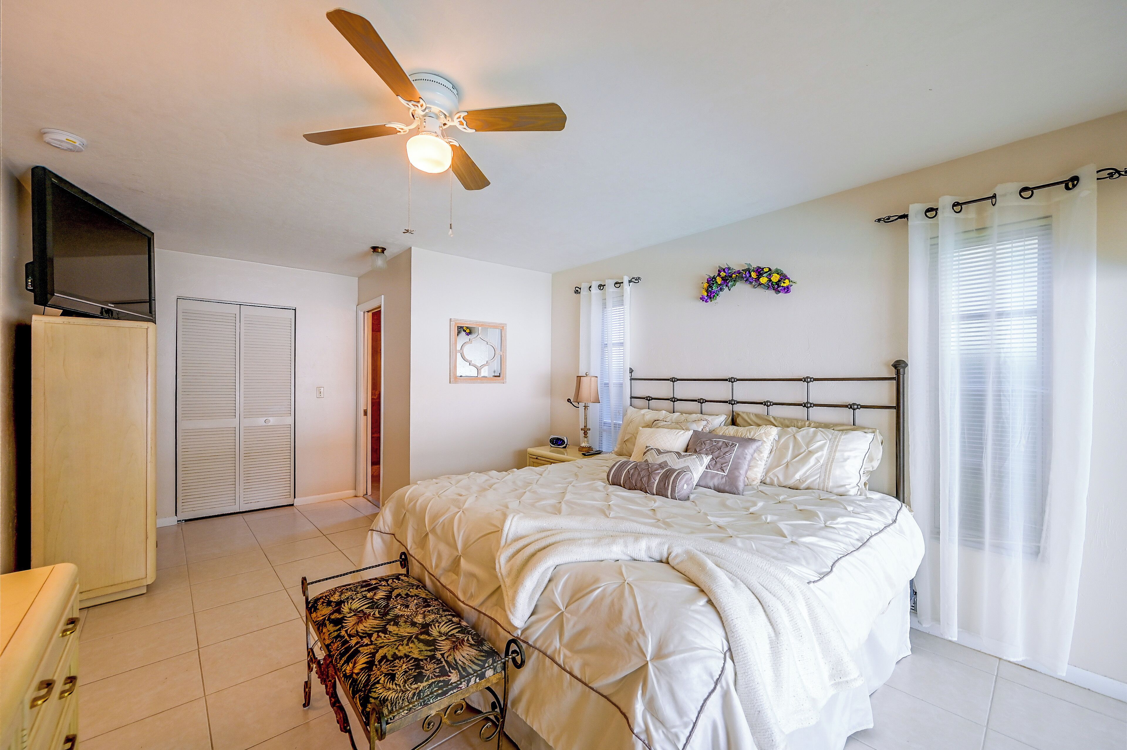 A bedroom with a bed, a nightstand, a chair, a ceiling fan, a TV, and a wardrobe.