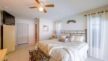 A bedroom with a bed, a nightstand, a chair, a ceiling fan, a TV, and a wardrobe.