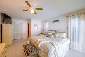 A bedroom with a bed, a nightstand, a chair, a ceiling fan, a TV, and a wardrobe.