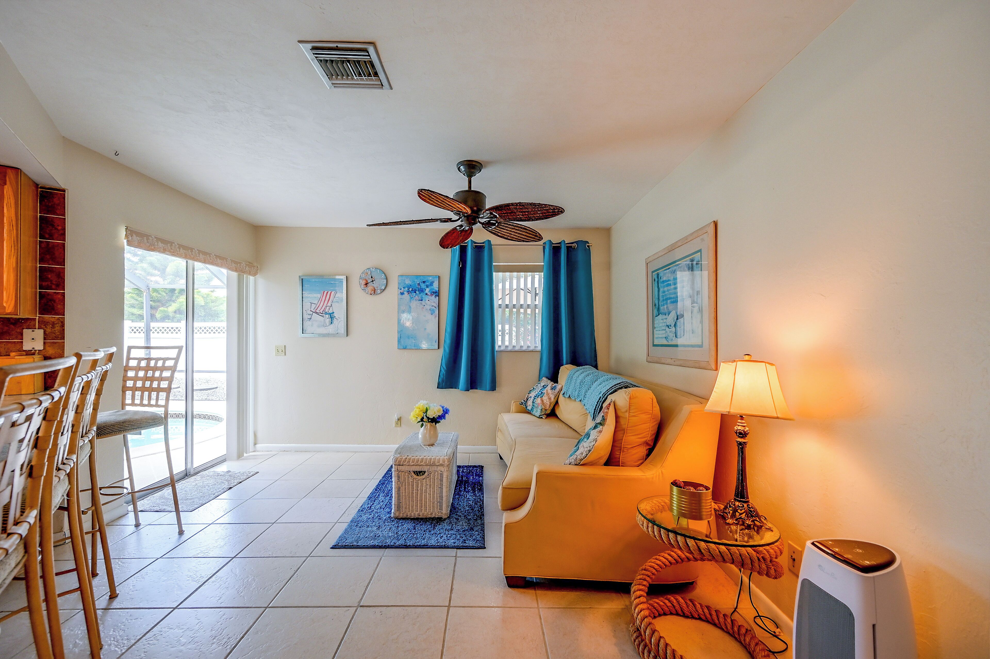 A living room with a sofa, a dining table, chairs, a ceiling fan, and a TV.