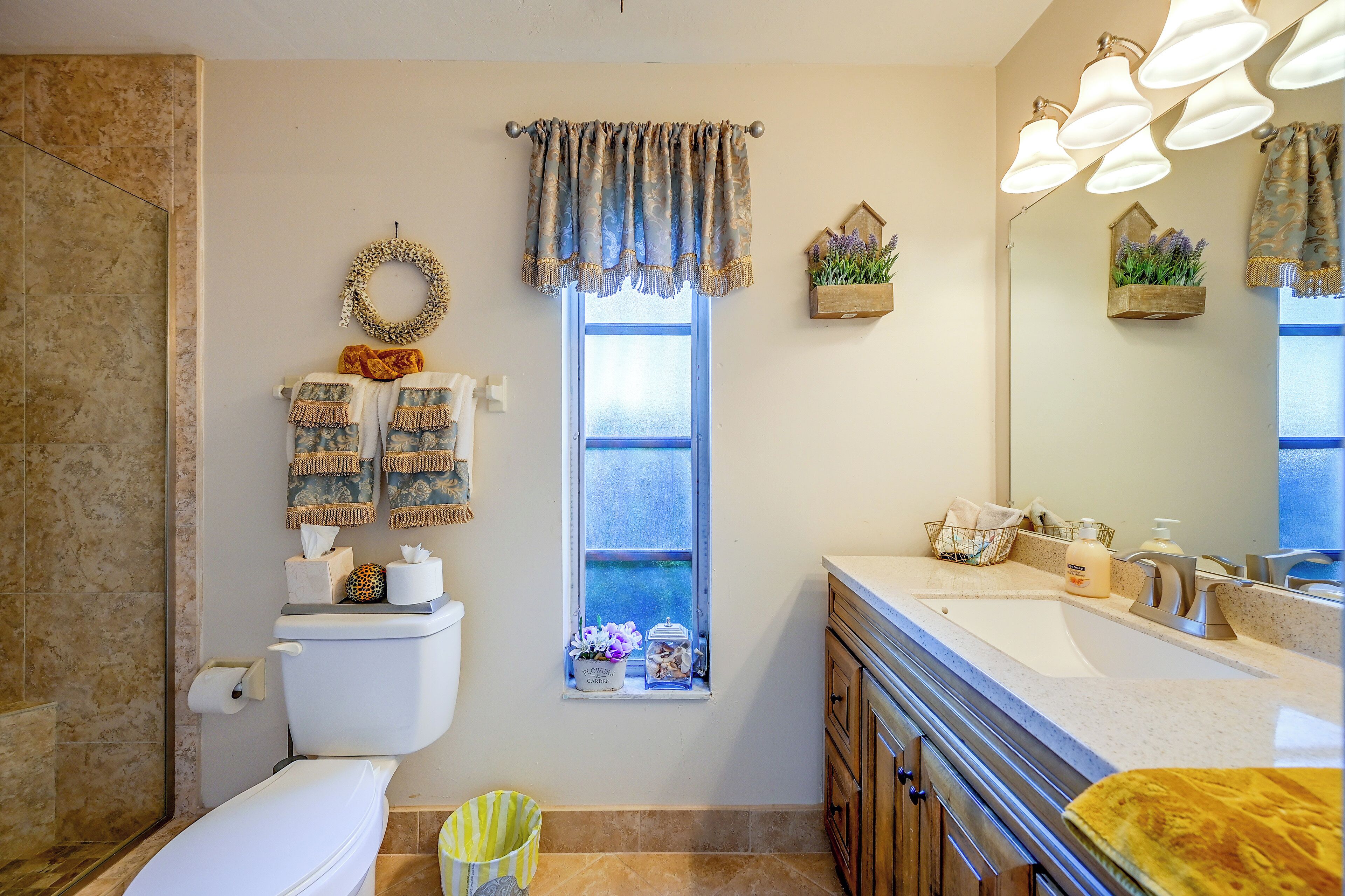 A bathroom with a toilet, sink, and window. There are towels and a basket on the wall.