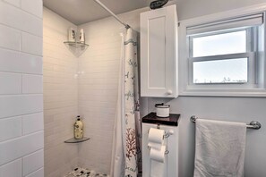 Een badkamer met witte betegelde wanden, een douche met glazen deur, een toilet met papieren handdoekhouder en een handdoekrek.