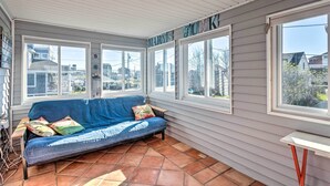 A covered porch with a blue sofa, large windows, and a view of the neighborhood.