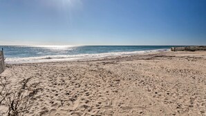 A sandy beach with footprints, a wooden fence, and a clear blue sky.