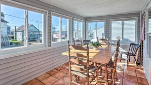 A covered patio with a wooden table and chairs, large windows, and a view of neighboring houses.