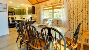A dining area with a wooden table and chairs, a kitchen in the background, and a window with a view of trees. - 3 Mi to Slopes! Poconos Chalet w/ Hot Tub & Sauna (Lake Harmony)