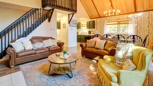A spacious living room with a brown leather sofa, a yellow armchair, and a coffee table. A wooden staircase with a railing leads to an upper level. - 3 Mi to Slopes! Poconos Chalet w/ Hot Tub & Sauna (Lake Harmony)
