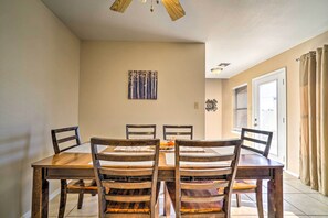 A dining area with a wooden table and chairs, a painting on the wall, and a window with blinds.