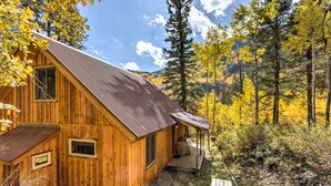 Una cabaña de madera con porche, rodeada de follaje otoñal y un paisaje montañoso.