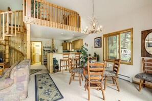 A spacious living area with a high ceiling, a dining table surrounded by chairs, a staircase leading to an upper level, and a view of the outdoors through large windows. - 'marble Hideaway' Cabin w/ Mountain Views + Deck! (Carbondale)