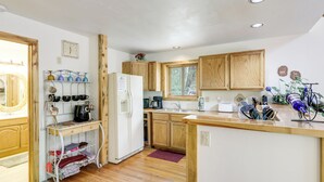 Una cocina con armarios de madera, un refrigerador, una cafetera y una ventana con vista a árboles.
