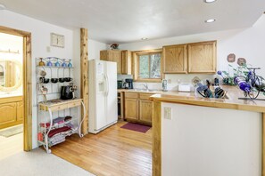 Una cocina con armarios de madera, un refrigerador, una cafetera y una ventana con vista a árboles.