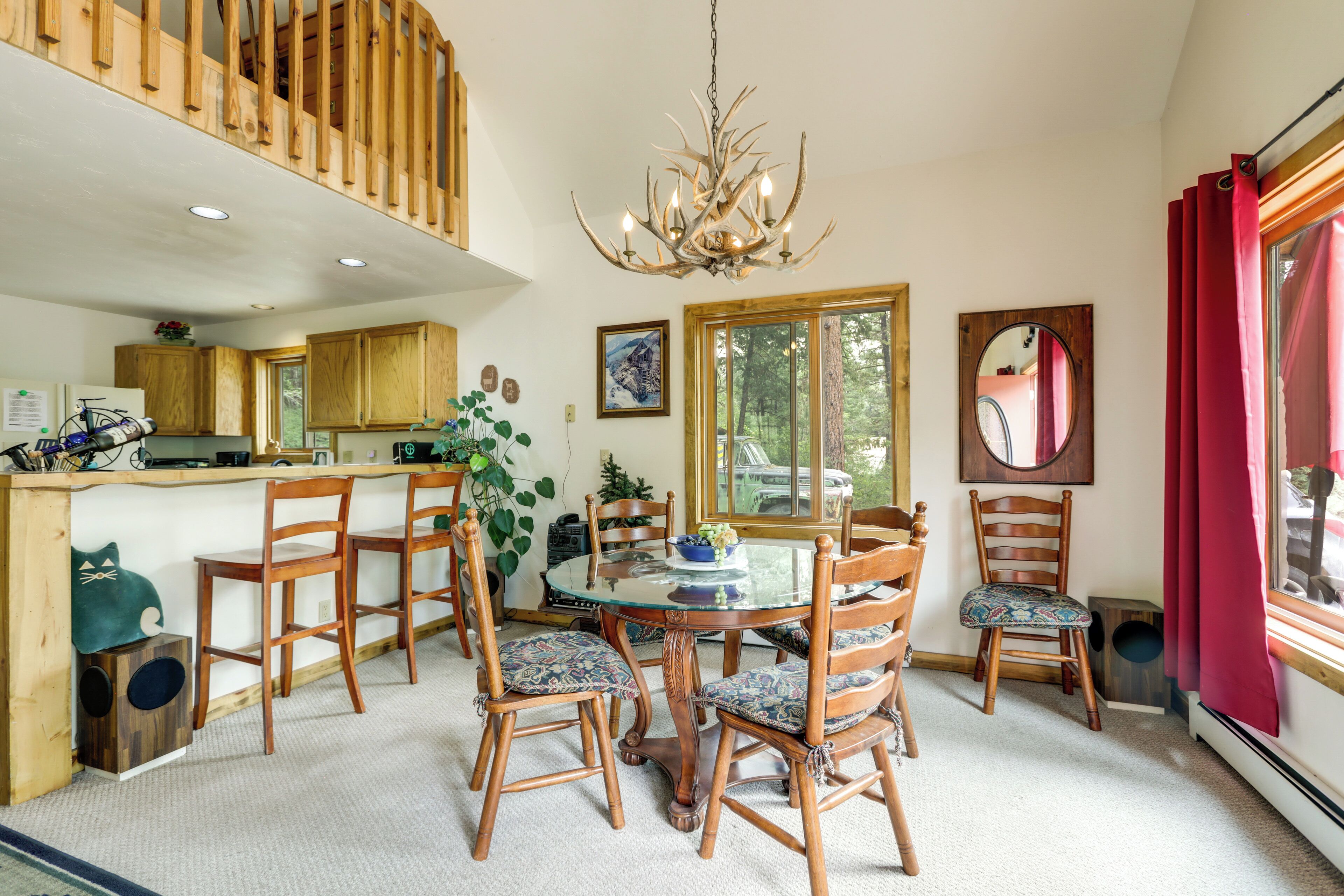 A dining area with a glass table surrounded by wooden chairs, a chandelier, and a view of the outdoors through large windows.