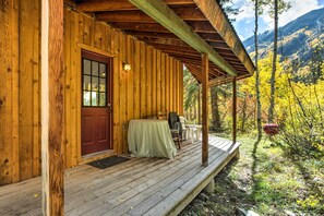 Eine Holzhütte mit Veranda, Tisch und Stühlen sowie Blick auf Herbstlaub und Berge.