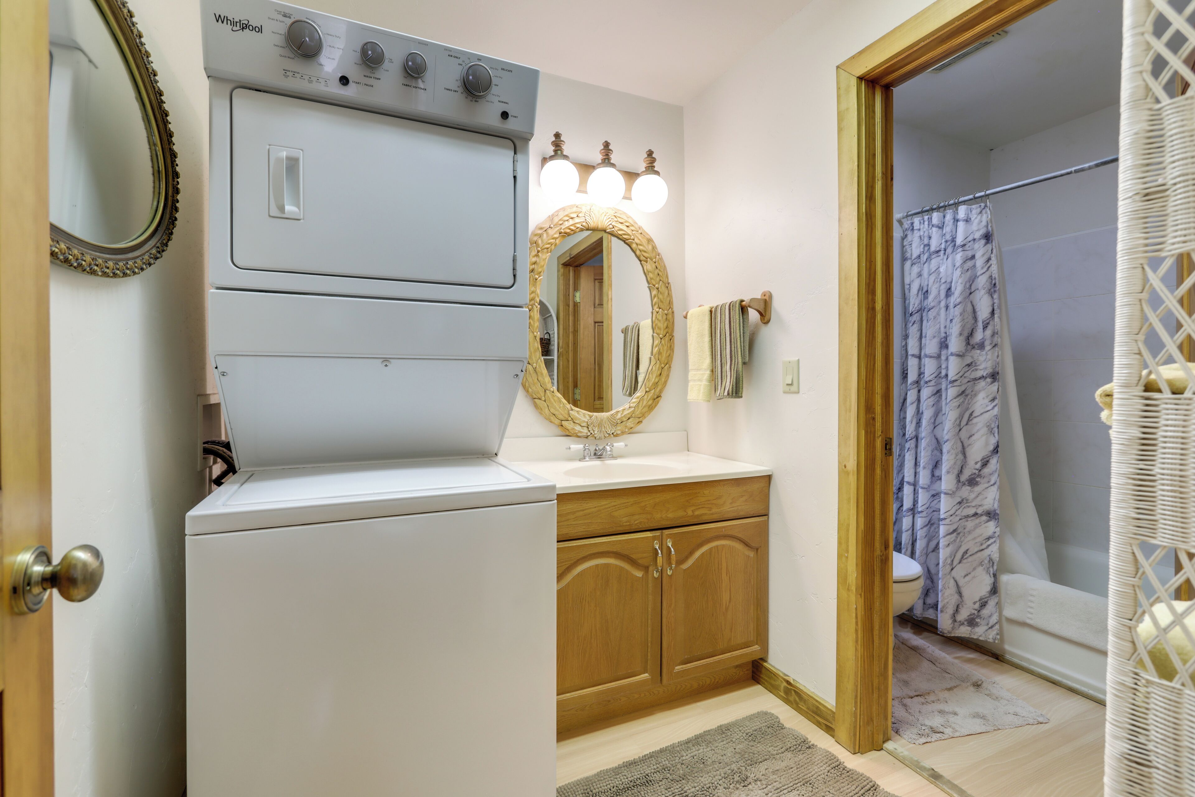 A bathroom with a washing machine, wooden cabinets, a mirror, and a shower curtain.