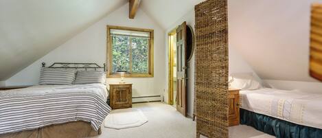 A bedroom with two beds, a window, a door, and a small bedside table.