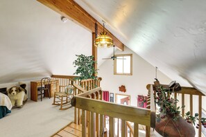 Un dormitorio estilo loft con una escalera de madera, un perro, una mecedora y una planta colgante.