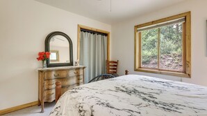 A bedroom with a bed, a dresser, a chair, a mirror, and a window with a view of trees. - 'marble Hideaway' Cabin w/ Mountain Views + Deck! (Carbondale)