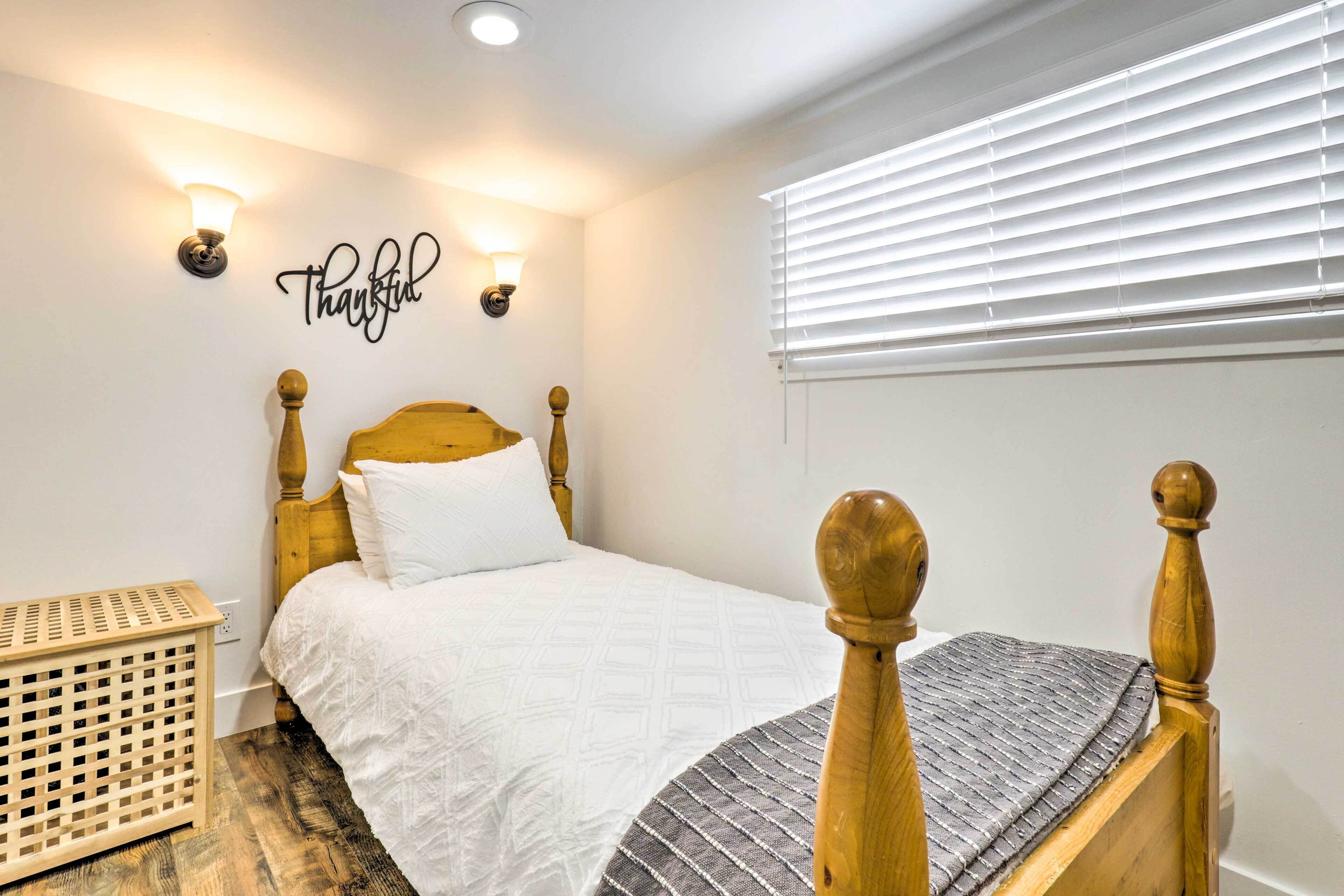 A neatly arranged bedroom with a wooden bed, a wall-mounted light fixture, and a window with blinds.
