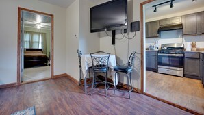 Une cuisine compacte dotée d’un four encastré, un coin repas avec une table et des chaises, et un téléviseur fixé au mur.