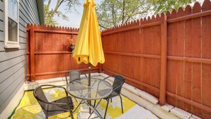 Une terrasse avec une table ronde et deux chaises, un parasol jaune et une clôture en bois.
